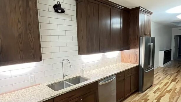 A modern kitchen with dark wooden cabinets, a granite countertop, stainless steel appliances, and a herringbone wood floor.