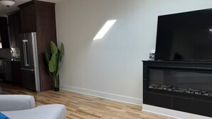 A modern living room with a grey sofa set, a flat-screen TV mounted on the wall, and a wooden floor.