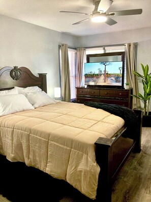 Ein Hotelzimmer mit einem Bett, einem Fernseher, einem Deckenventilator und einem Fenster mit Vorhängen.