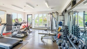 Ein Fitnessraum mit Laufbändern, Crosstrainern, einer Langhantelbank und einer Hantelbank.