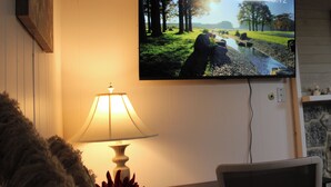 Seinälle asennettu televisio, jossa näkyy kaunis maisema, pöydällä oleva lamppu ja tuoli.