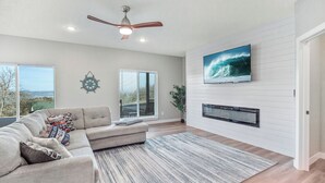 A spacious living room with a large sectional sofa, a ceiling fan, a mounted TV, and a fireplace. - Modern Lewis and Clark lake home with lake views and 3 min drive to the beach! (Crofton)
