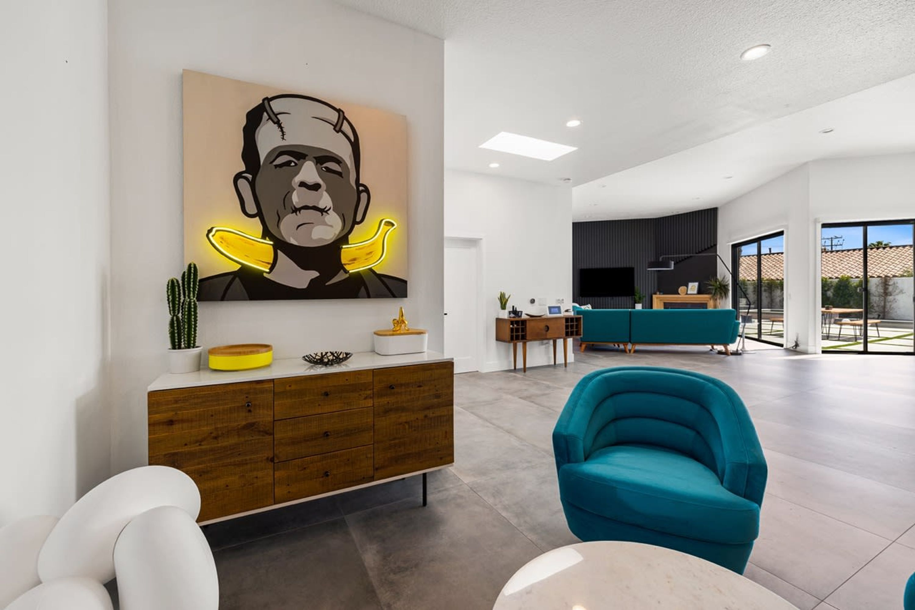 Un salon moderne agrémenté d’une grande œuvre d’art, d’un meuble en bois, d’un fauteuil turquoise et d’un coin repas à l’arrière-plan.