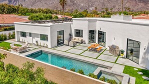 Ein modernes Haus mit Swimmingpool, Außenbereich zum Sitzen und Blick auf Berge.