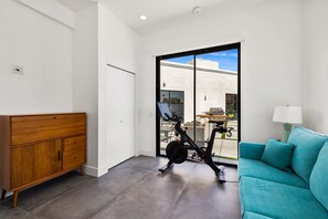A modern living room with a teal sofa, a wooden cabinet, and an exercise bike. - The Lighthouse- Monthly 4 bd 4 bth Pool Spa (Palm Springs)