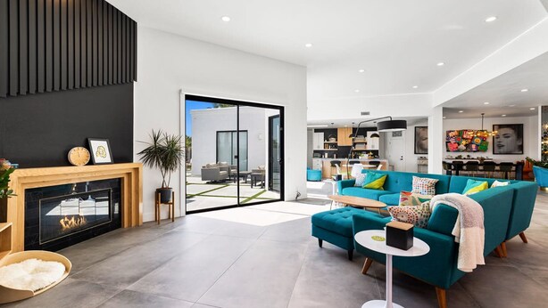 Ein modernes Wohnzimmer mit Kamin, Türkis-sofas und einem Essbereich, der durch eine Glastür sichtbar ist.