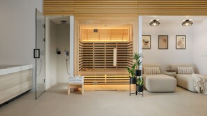 Une salle de spa moderne avec un sauna en bois, un coin salon comprenant un canapé et des coussins, ainsi qu'une petite table agrémentée d'une plante.