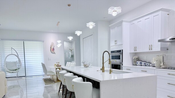 A modern kitchen with a central island, white cabinetry, and a hanging light fixture. - Delightful 4-bedroom 4 full bath and one Den house with AC and heater Lehigh  (Lehigh Acres)