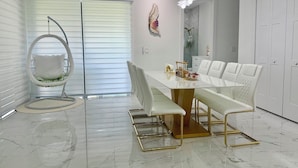 A modern dining room with a white marble table, white upholstered chairs, and a hanging chair with a cushioned seat. - Delightful 4-bedroom 4 full bath and one Den house with AC and heater Lehigh  (Lehigh Acres)