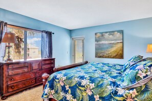 Ein Schlafzimmer mit Bett, Kommode, Fenster mit Jalousien und einem Bild an der Wand.