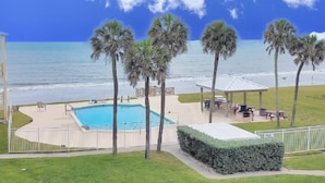 A pool area with palm trees, a gazebo, and a view of the ocean. - Monthly Stay Oceanside Condo — Heated Pool, on the Beach & Fire Pit! 🌴🌊 (Satellite Beach)