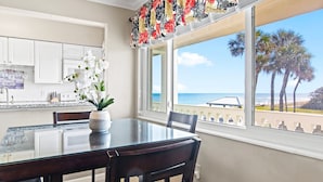 A dining area with a view of the ocean and palm trees. - Monthly Stay Oceanside Condo — Heated Pool, on the Beach & Fire Pit! 🌴🌊 (Satellite Beach)