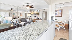 A spacious living area with a large granite island, a ceiling fan, and a dining area with a small table and chairs. - Monthly Stay Oceanside Condo — Heated Pool, on the Beach & Fire Pit! 🌴🌊 (Satellite Beach)
