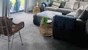 A modern living room with a grey sofa, a wicker chair, and a flat-screen TV.