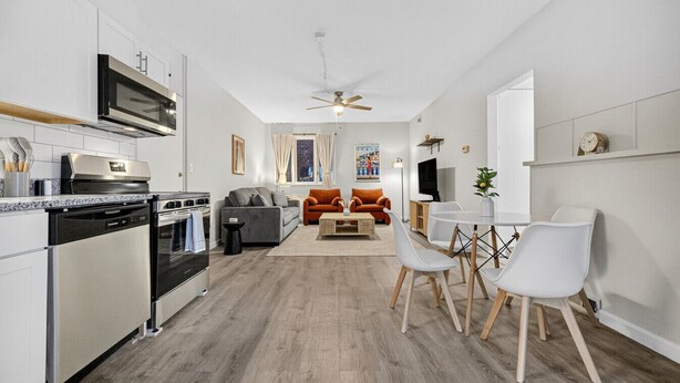 A modern kitchen with stainless steel appliances, a dining area with white chairs and a wooden table, and a living room with a sofa and orange armchairs. - Little Italy Gem | Patio | Free Parking (Cleveland)
