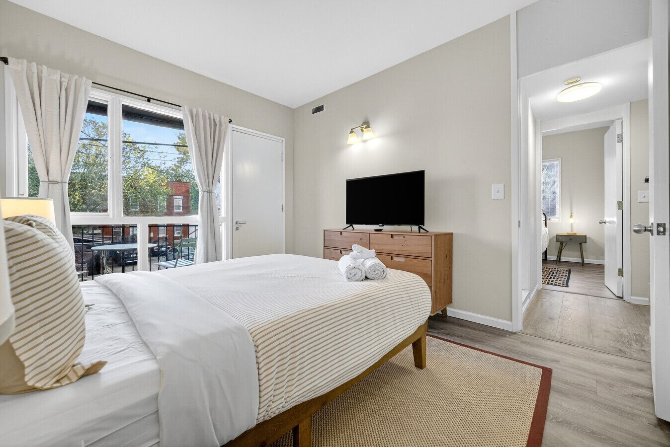 A bedroom with a bed, a TV on a wooden dresser, and a view of the outside.