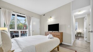 A bedroom with a bed, a TV on a wooden dresser, and a view of the outside. - Little Italy Gem | Patio | Free Parking (Cleveland)