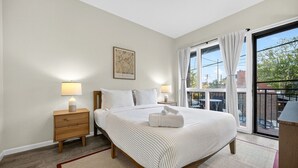 A bedroom with a large bed, two bedside tables with lamps, a window with curtains, and a view of the outside. - Little Italy Gem | Patio | Free Parking (Cleveland)