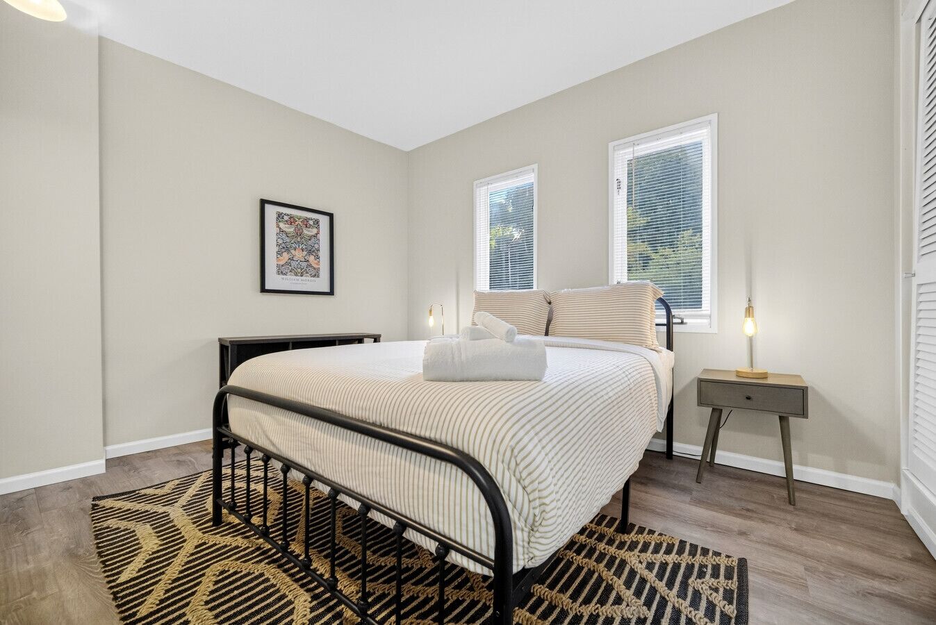 Un dormitorio con cama, mesita de noche, lámpara y un cuadro en la pared.