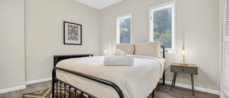 Un dormitorio con cama, mesita de noche, lámpara y un cuadro en la pared.