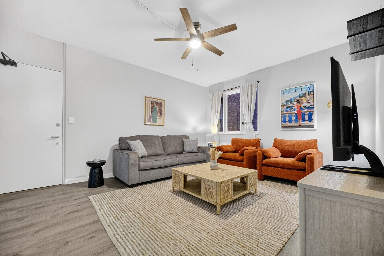 Ein modernes Wohnzimmer mit einem grauen Sofa, einem orangen Sofa, einem Couchtisch, einem Fernseher und einem Deckenventilator.