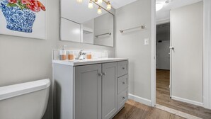 A modern bathroom with a toilet, sink, and mirror. There is a wooden floor and a hallway leading to another room. - Little Italy Gem | Patio | Free Parking (Cleveland)