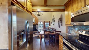 A modern kitchen with stainless steel appliances, wooden cabinets, and a dining area with a chandelier. - Walk to Slopes | Master ensuite | Snowfire 303B (Angel Fire)