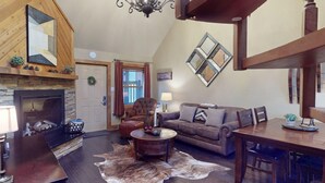 A cozy living room with a fireplace, a leather armchair, a sofa, and a dining table. - Walk to Slopes | Master ensuite | Snowfire 303B (Angel Fire)