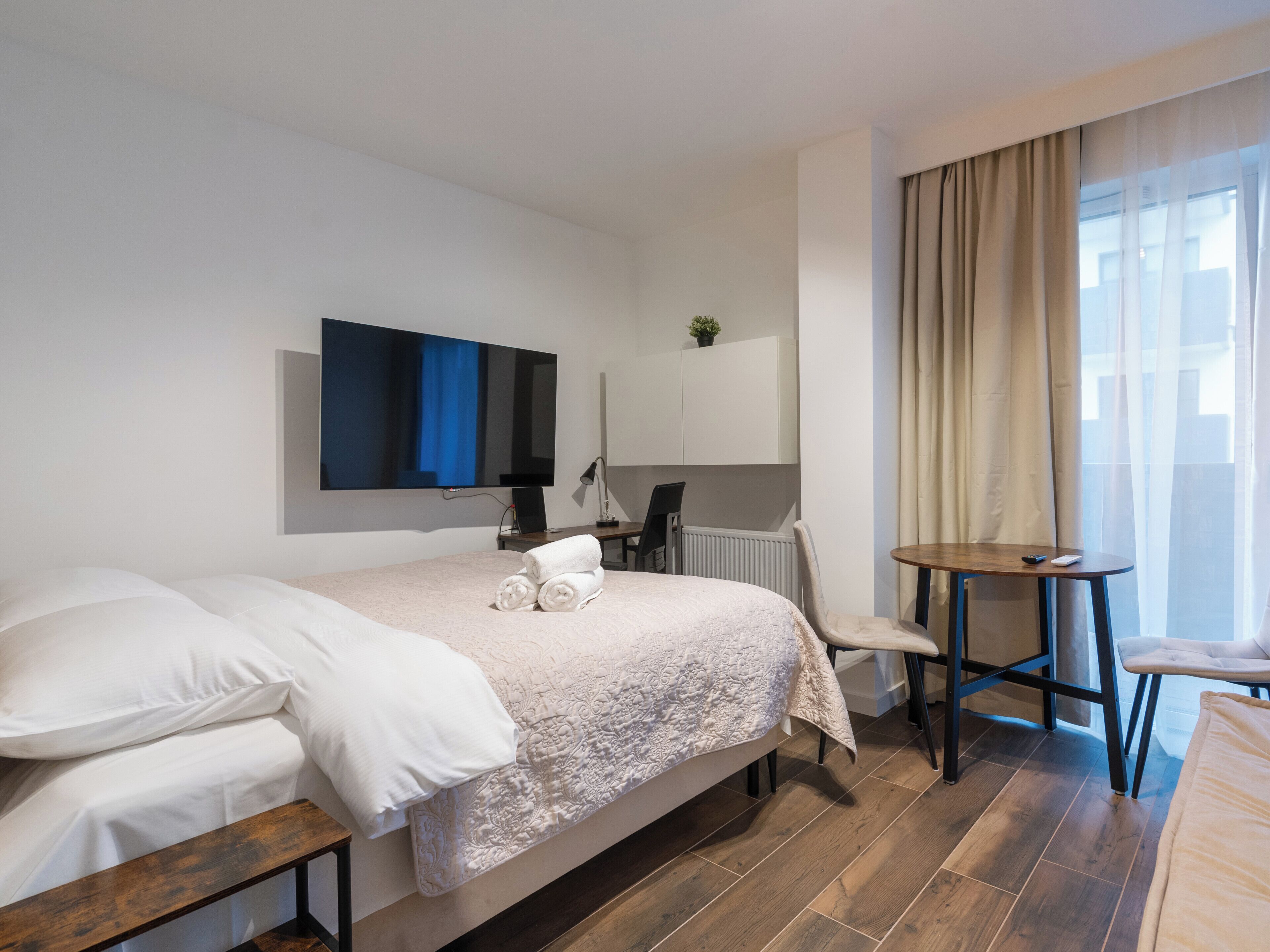 Habitación de hotel con cama, escritorio, silla, televisor y ventana con cortinas.