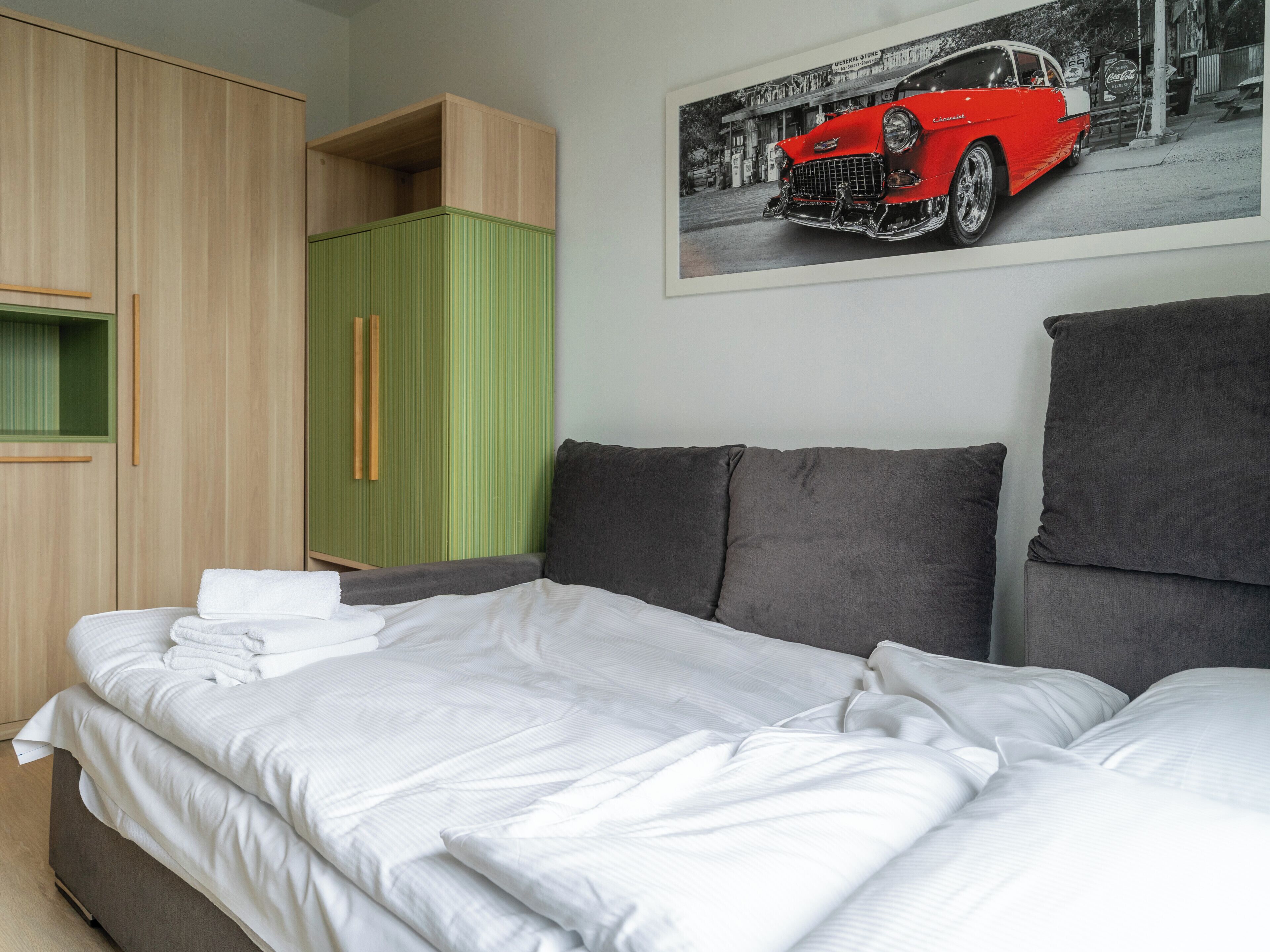 Een slaapkamer met een bed, een groene kast en een aan de muur hangend beeld van een oldtimer.