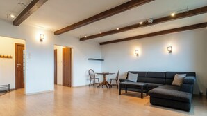 Ein großzügiger Wohnbereich mit grauem Sofa, Holzboden, freiliegenden Holzbalken und einem Esstisch mit Stühlen.
