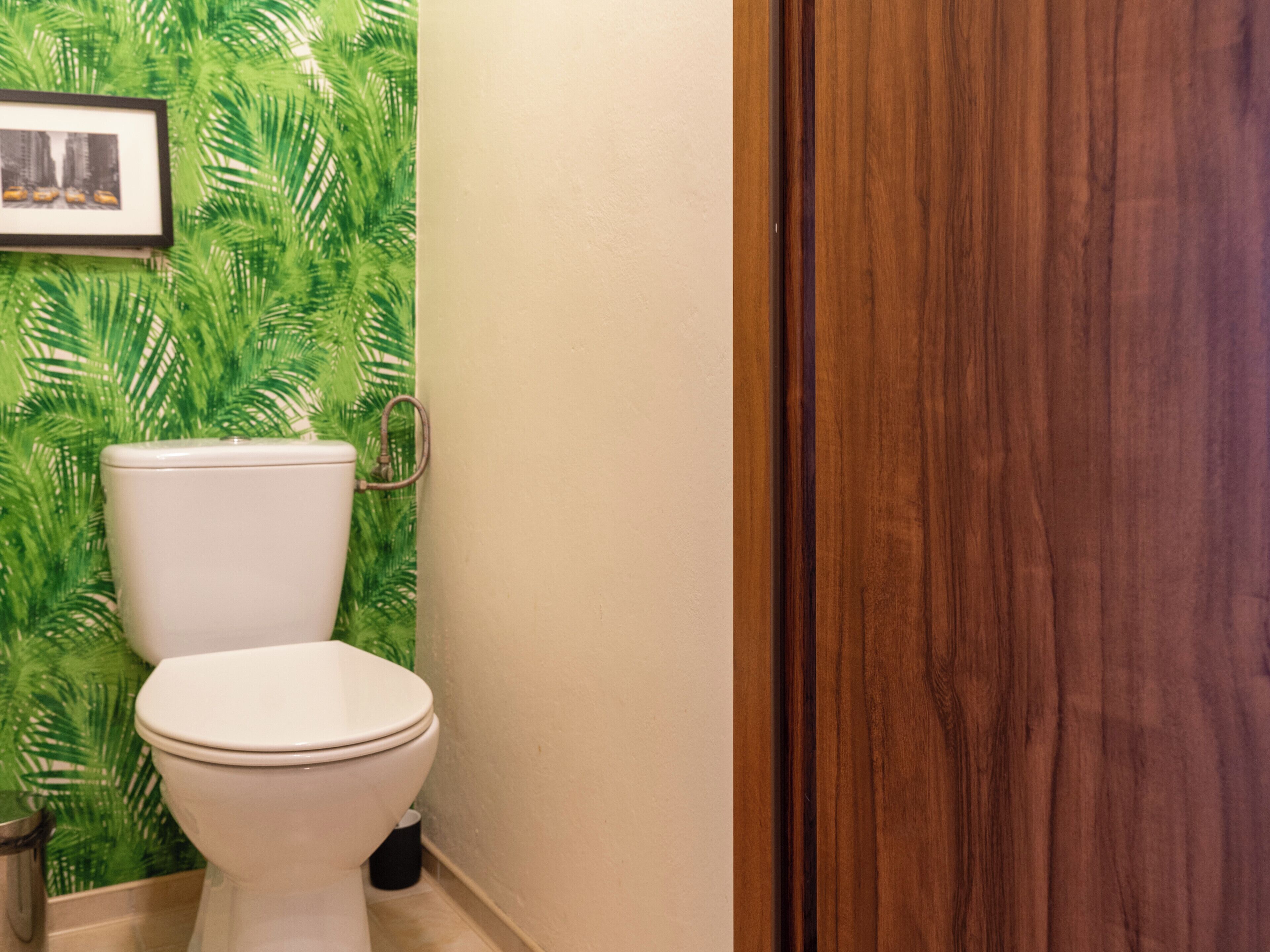 A bathroom with a toilet, a wooden door, and a wall with a green leaf pattern.