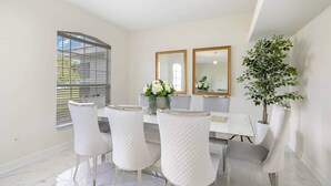 Un coin repas avec une table blanche, quatre chaises, deux miroirs et une plante en pot.
