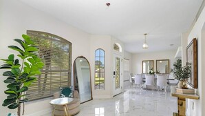 Une pièce spacieuse avec un grand miroir, un coin repas avec des chaises blanches et un sol en marbre.