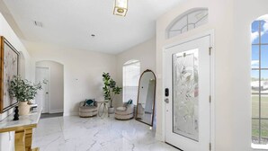 Un hall spacieux doté d’un sol en marbre, d’une porte blanche ornée d’un panneau de verre décoratif et d’un grand miroir.