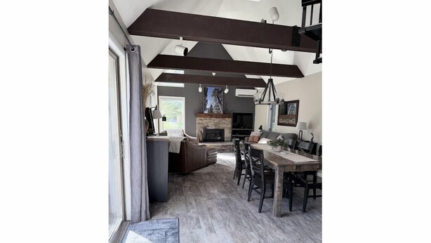 A modern kitchen with a stone fireplace, wooden ceiling beams, and a dining area with a table and chairs.