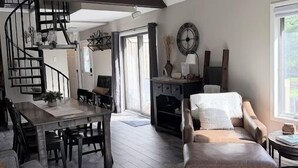 A spacious loft with a high ceiling, a spiral staircase, a dining area, a sofa, and a fireplace.