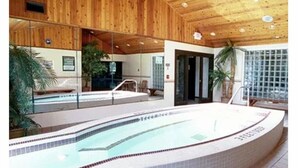 An indoor swimming pool with a wooden ceiling and tiled walls, surrounded by glass windows.