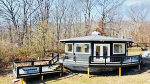 Une petite cabane à un seul étage, dotée d’une terrasse clôturée et d’un escalier menant à l’entrée.