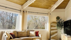 Un loft spacieux avec de hauts plafonds, des poutres apparentes, un grand canapé, une table basse en bois, un téléviseur et un escalier en colimaçon.