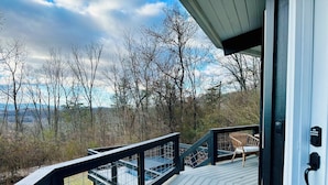 Une terrasse en bois avec une rambarde en verre donnant sur une zone boisée.
