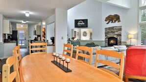 Ein Essbereich mit Holztisch und -stühlen, eine Küche im Hintergrund, ein Kamin und ein an der Wand befestigter Fernseher, der 'simple vacation rentals' anzeigt.
