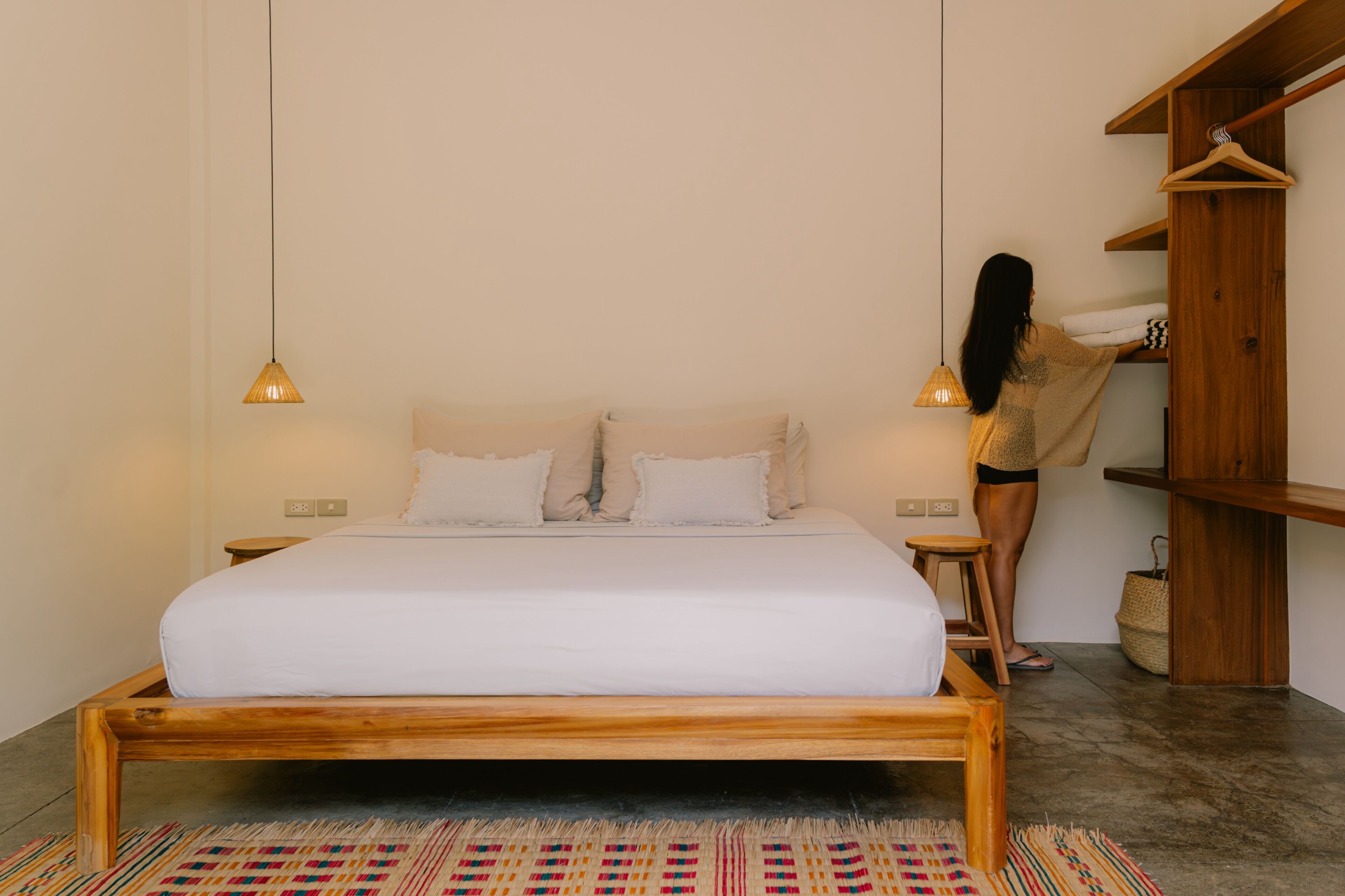 Un letto con struttura in legno, una lampada a sospensione e un piccolo sgabello.
