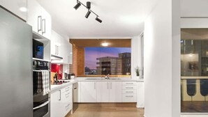 Una cocina moderna con armarios blancos, un refrigerador de acero inoxidable, un horno y una ventana con vistas a la ciudad.
