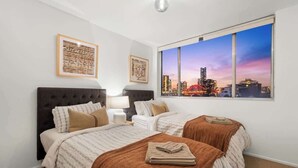 Habitación de hotel con dos camas, vista a la ciudad y obras de arte enmarcadas en las paredes.