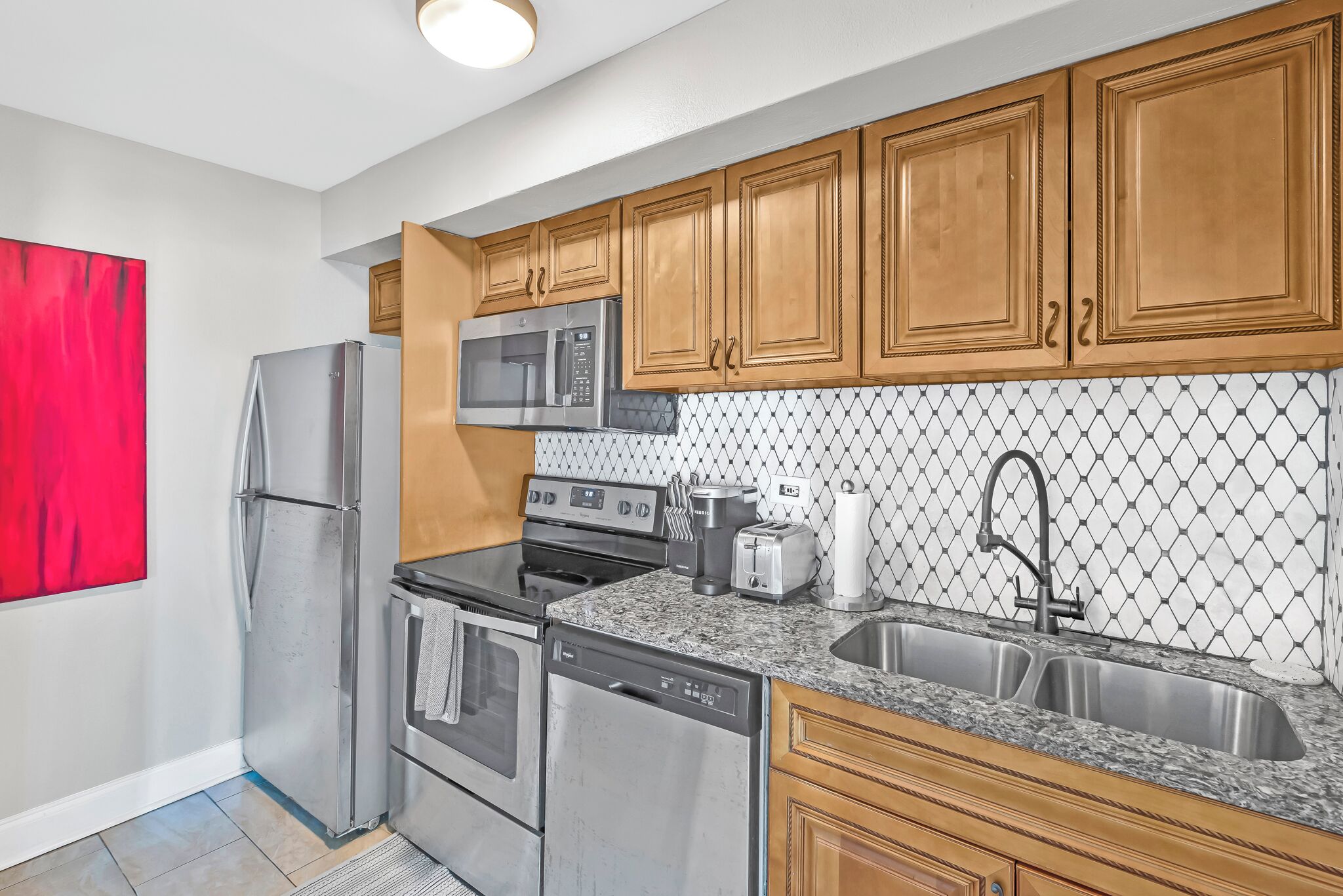 A modern kitchen with stainless steel appliances, wooden cabinets, and a granite countertop.