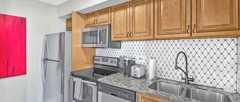 A modern kitchen with stainless steel appliances, wooden cabinets, and a granite countertop.