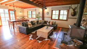 A spacious living room with a wooden ceiling, a large L-shaped sofa, a coffee table, and a stone fireplace. - Nala Lodge - Peaceful Alpine Retreat (Harrietville)