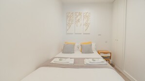 Een keurig opgemaakt slaapkamer met een bed, kussens, een nachtkastje en wanddecoratie.