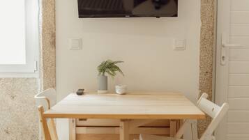 A wooden dining table with chairs, a potted plant, a small white container, and a remote control.